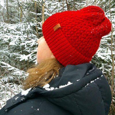 Девушка в красной вязаной шапке с кожаной биркой среди заснеженных деревьев